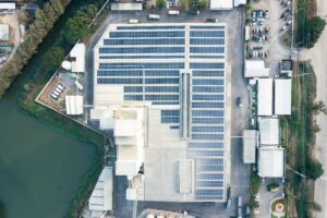 Birds eye view of building with solar panels installed on roof. Surrounded by water and other industrial buildings.