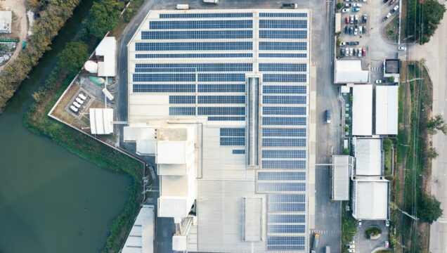 Birds eye view of building with solar panels installed on roof. Surrounded by water and other industrial buildings.